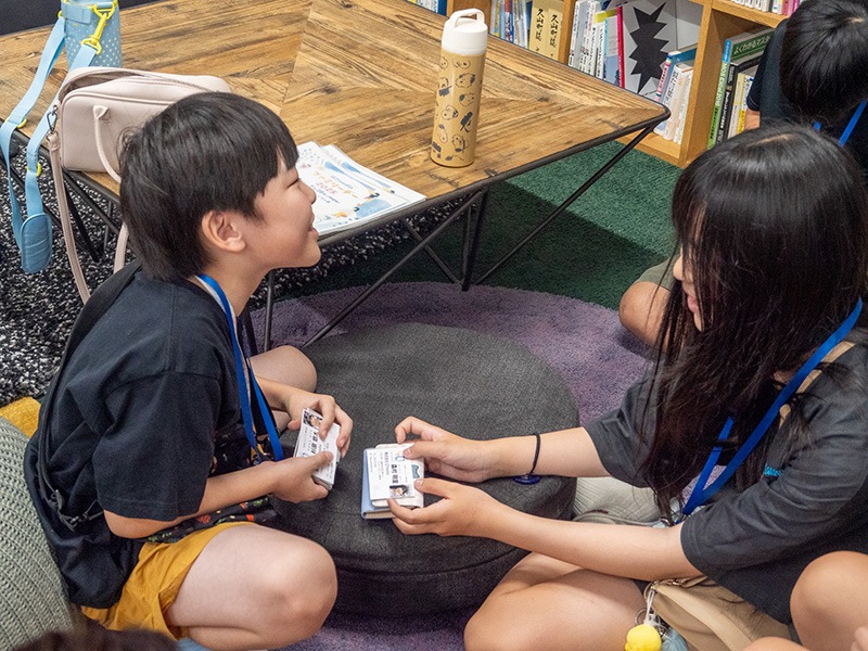 写真：小学生中学年くらいの男の子と女の子が名刺交換しているようす